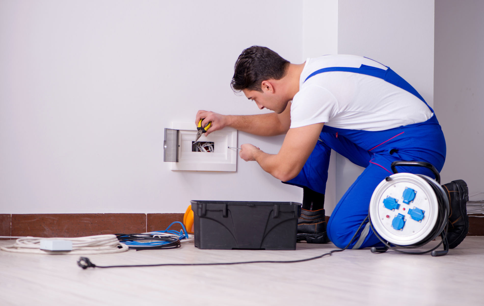 A man is kneeling down fixing an electrical outlet on a wall.