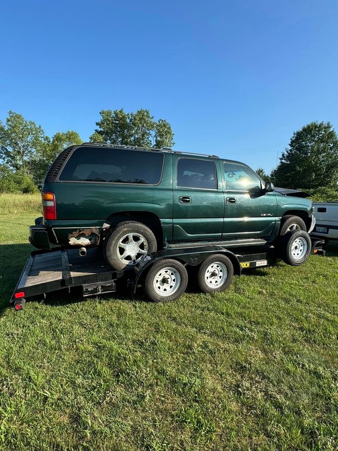A green suv is being towed by a trailer in a grassy field.