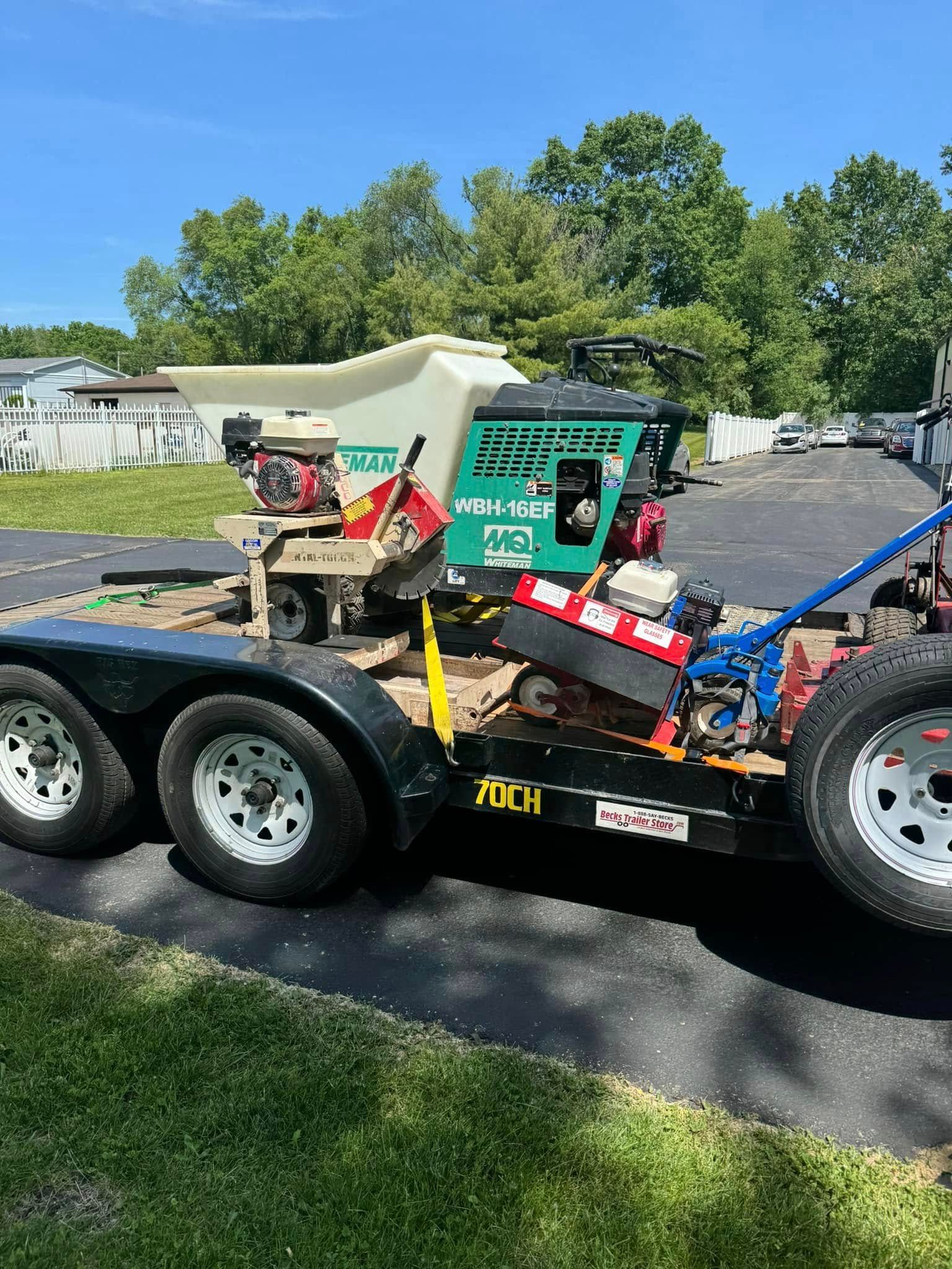 A trailer with a tractor on it is parked on the side of the road.
