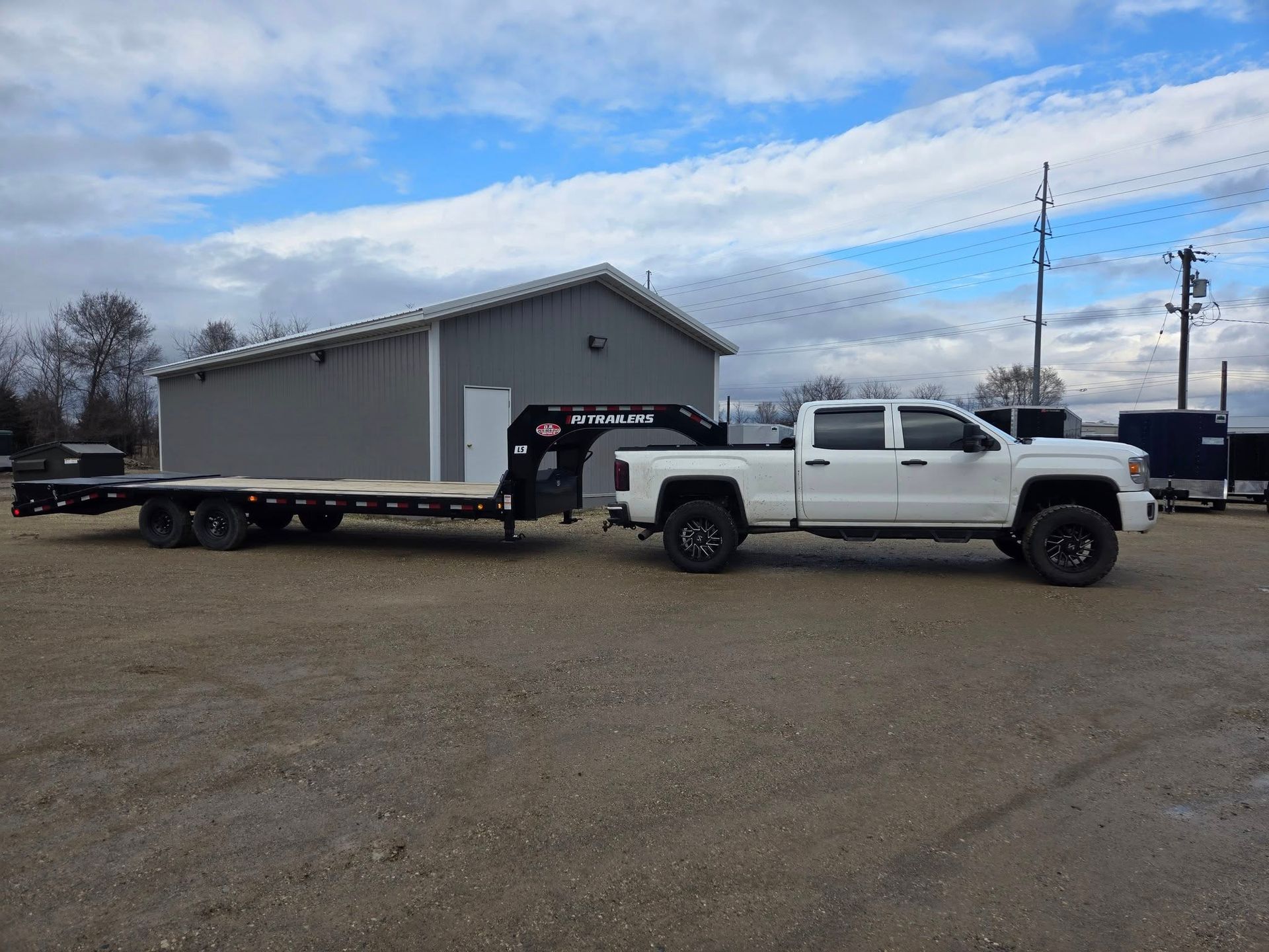 A white truck is towing a flatbed trailer in a parking lot.