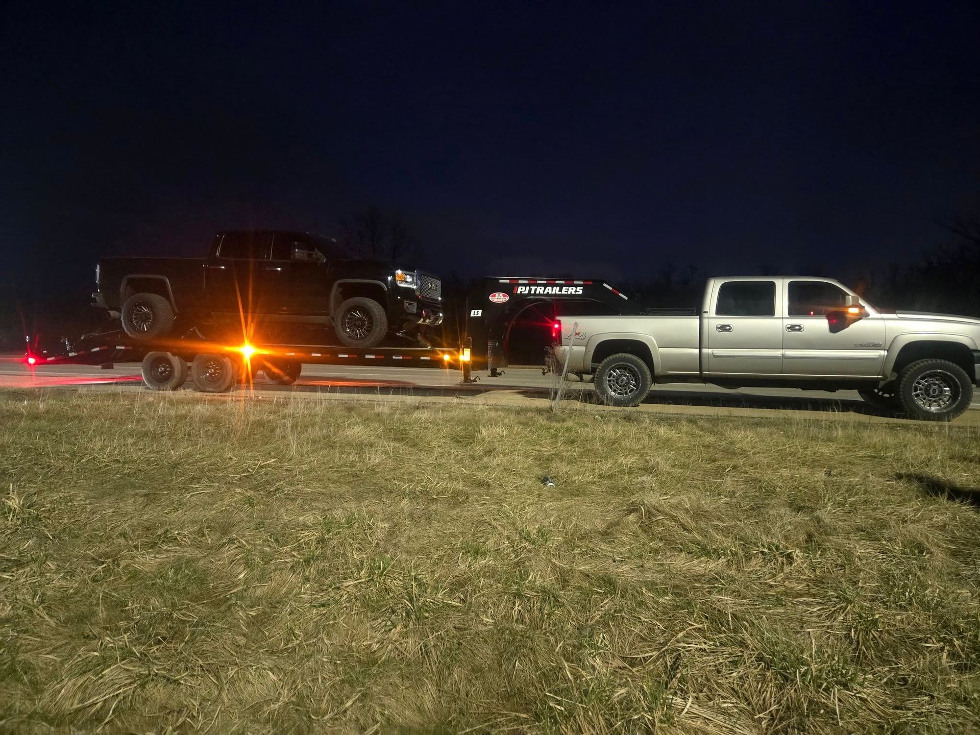 A white truck is towing a black truck on a trailer.