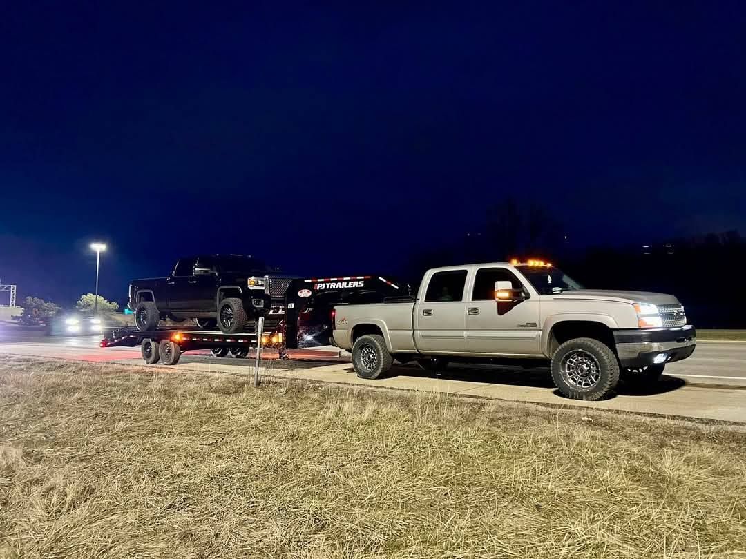 A truck is towing a trailer with a jeep on it.
