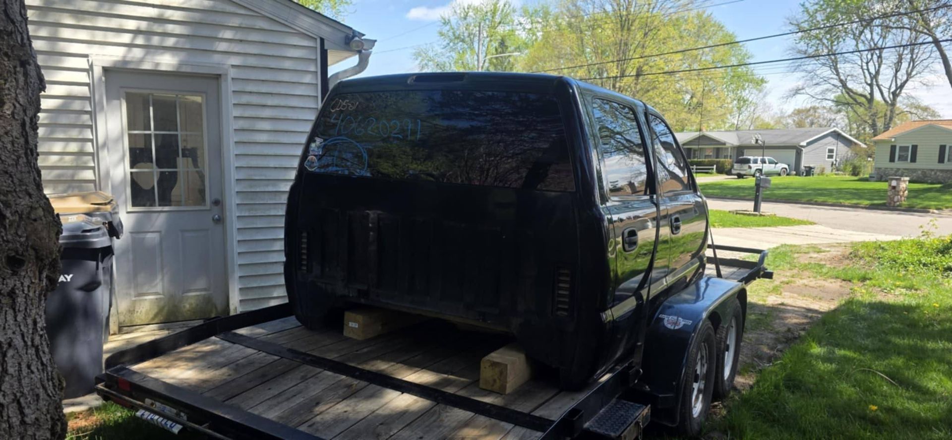 A black truck is sitting on top of a trailer in front of a house.
