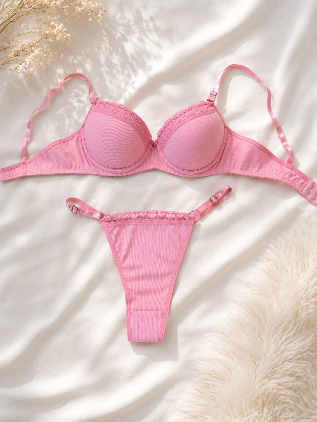 Conjunto de lencería rosa con sujetador y tanga a juego sobre un fondo blanco esponjoso.