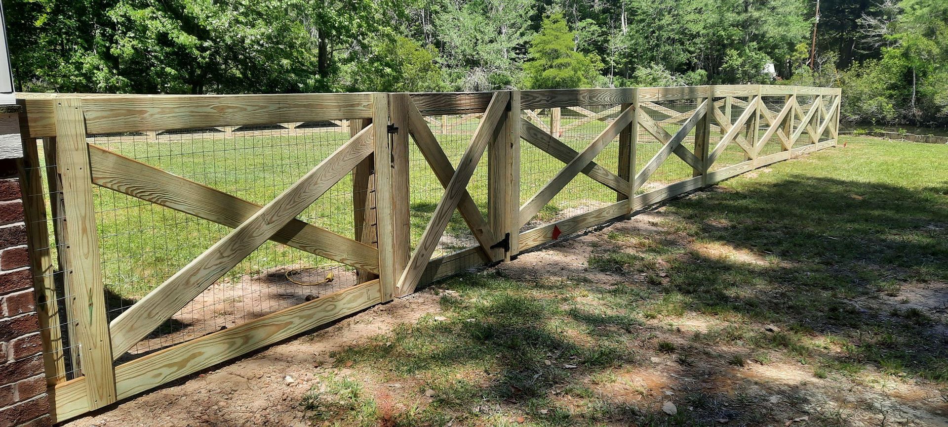 Wooden fence lining a grassy path through a sunlit wooded area