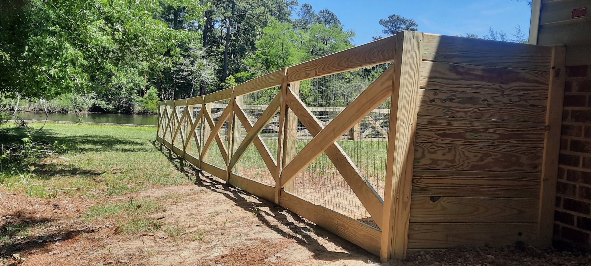 Wooden fence with crisscross rails along a dirt path in a sunny wooded area