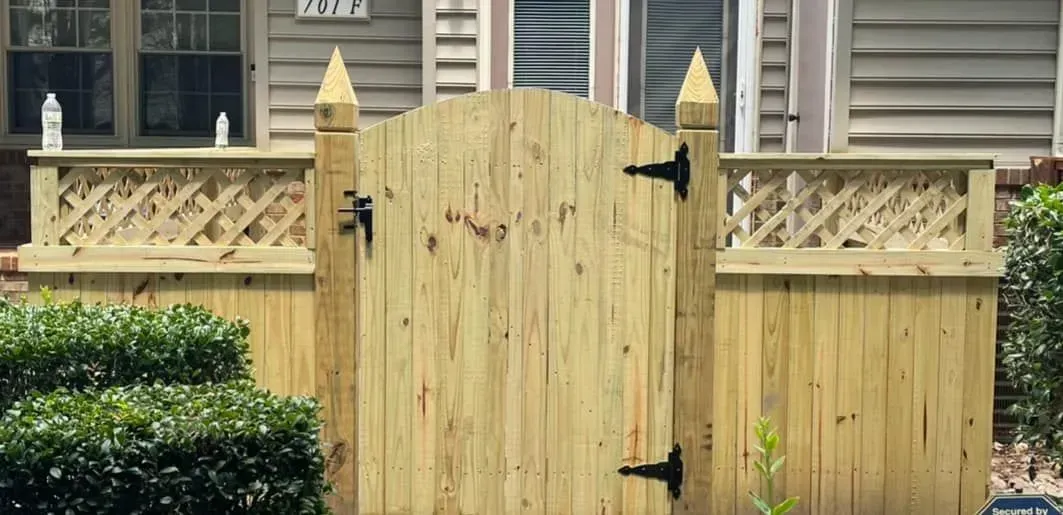Wooden gate with black hinges and decorative lattice fence.