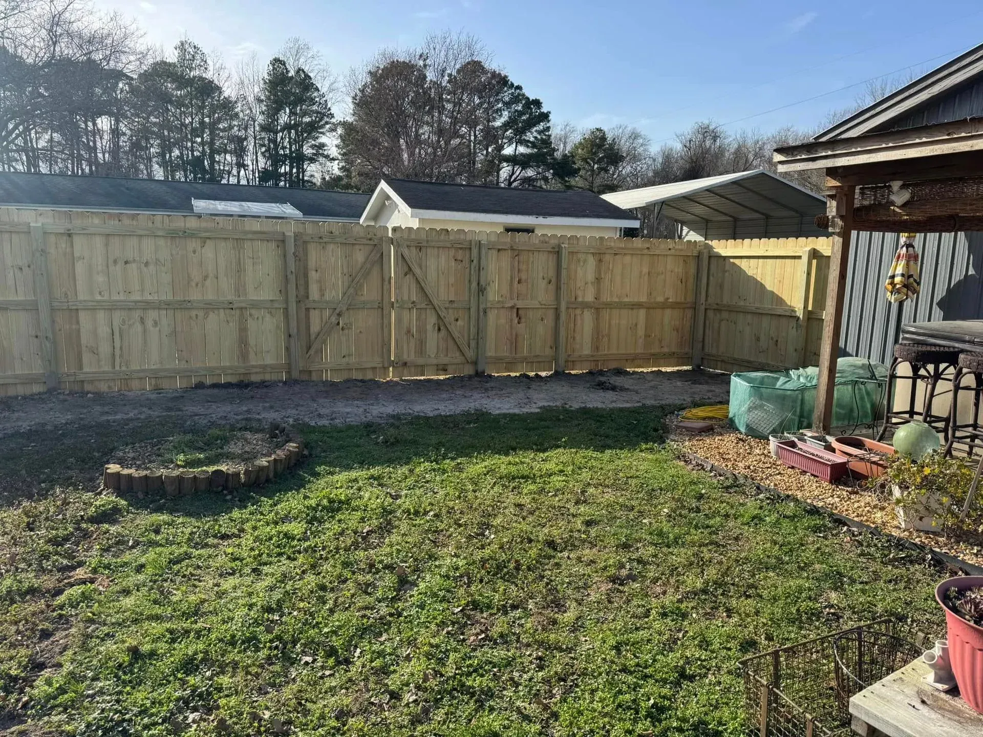 A wooden fence encloses a backyard with green grass. A gate is in the center.