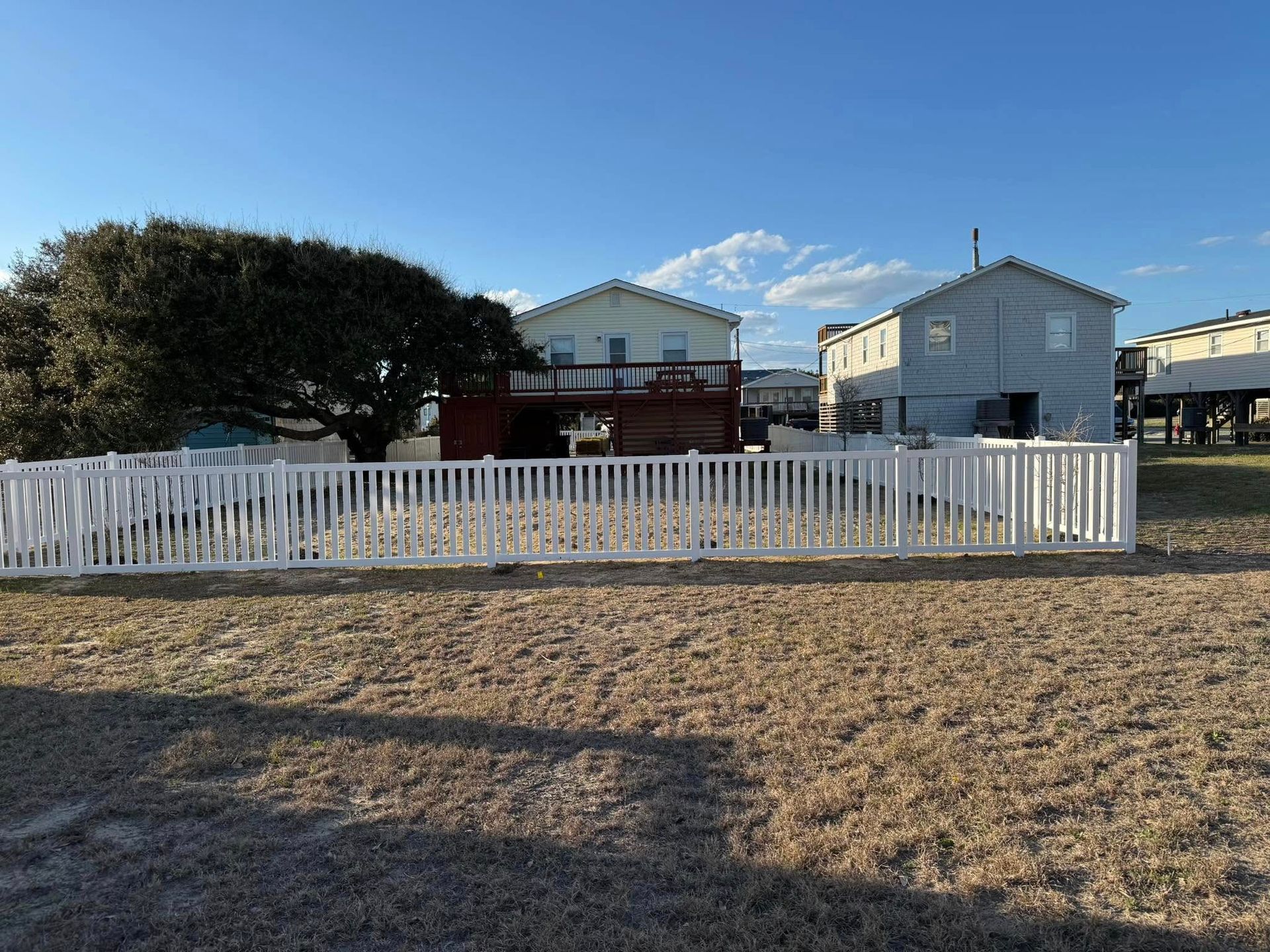 White picket fence surrounds houses under a blue sky, on a grassy field.