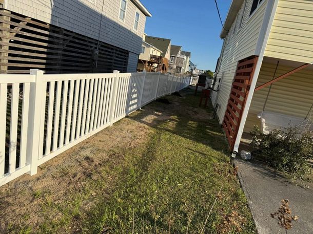 White picket fence along a grassy strip between two houses on a sunny day. White picket fence along a grassy strip between two houses on a sunny day.