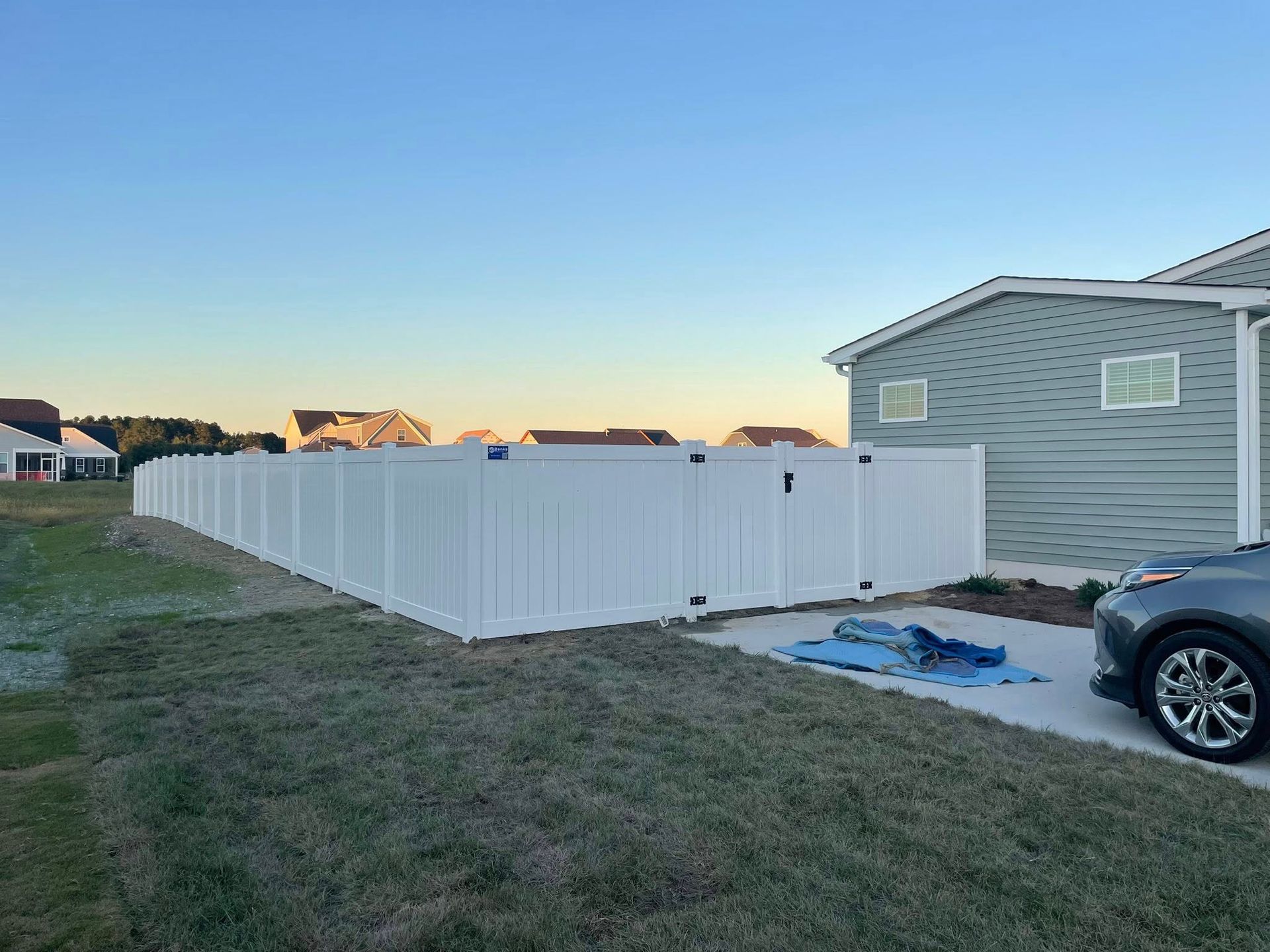 White vinyl fence around a house in a residential area. A car is parked in the driveway.