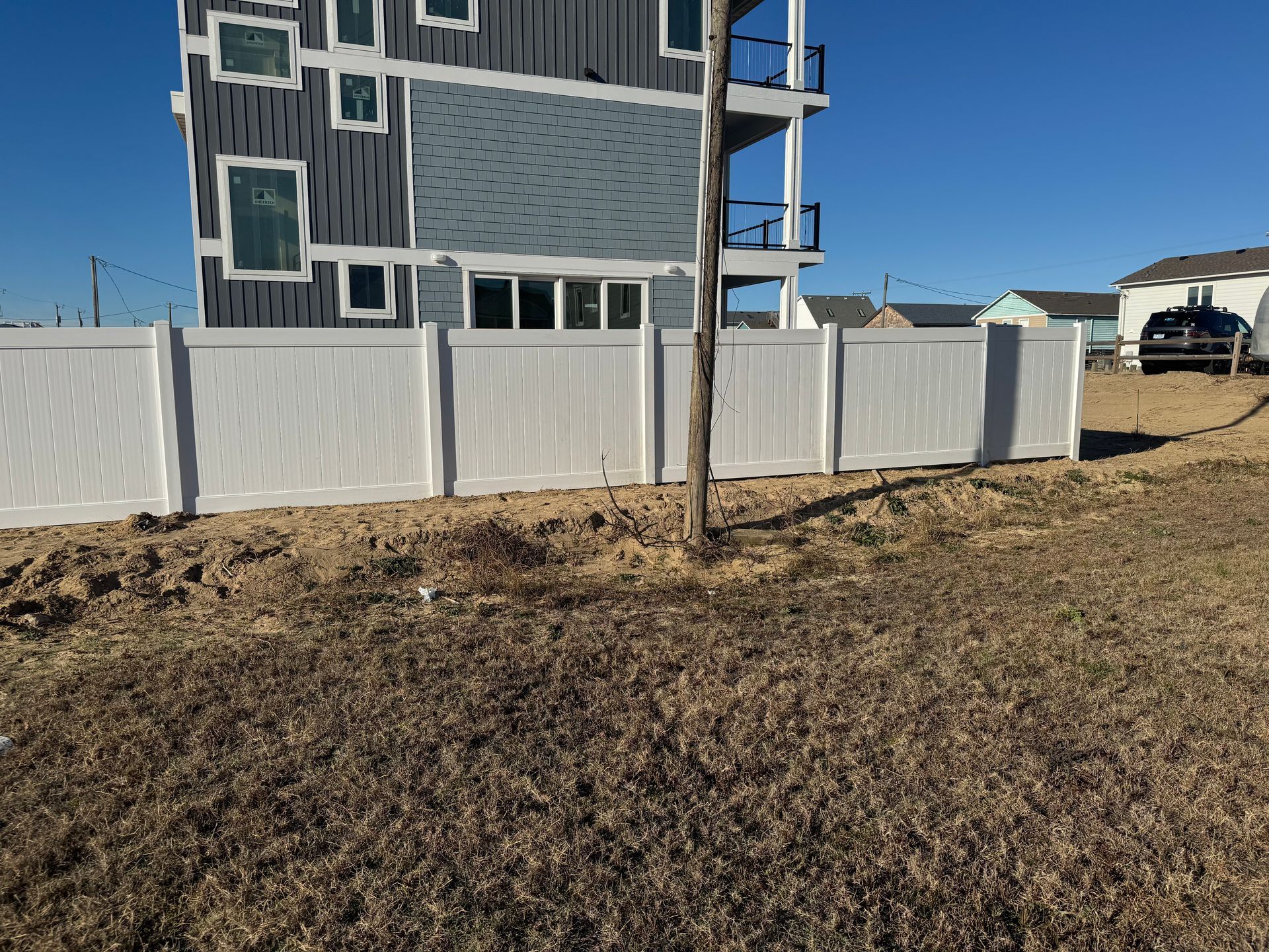 White fence in front of a blue house under a clear sky. Brown ground in the foreground.