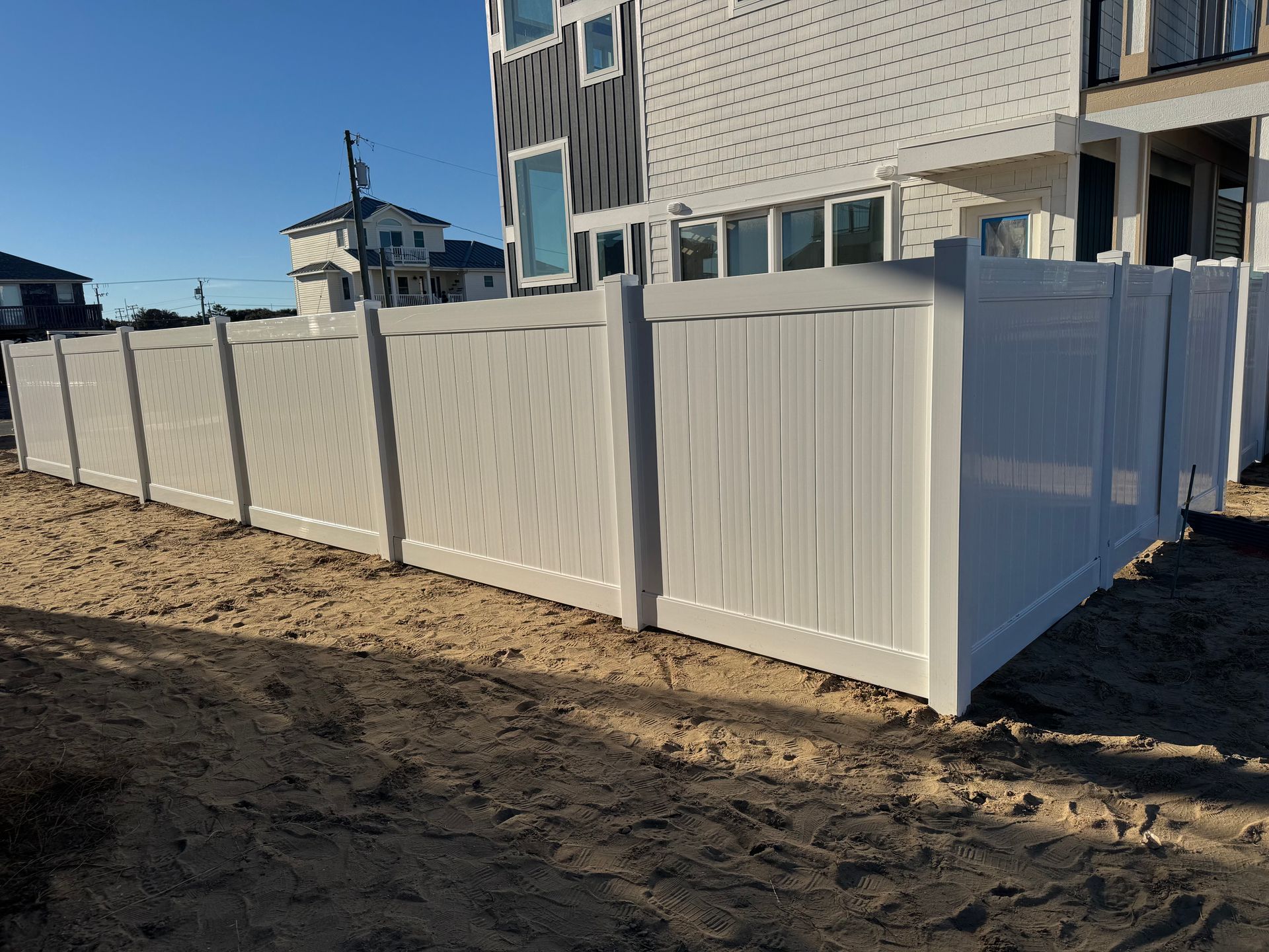 White vinyl fence along a dirt ground, with a modern building in the background under a blue sky.