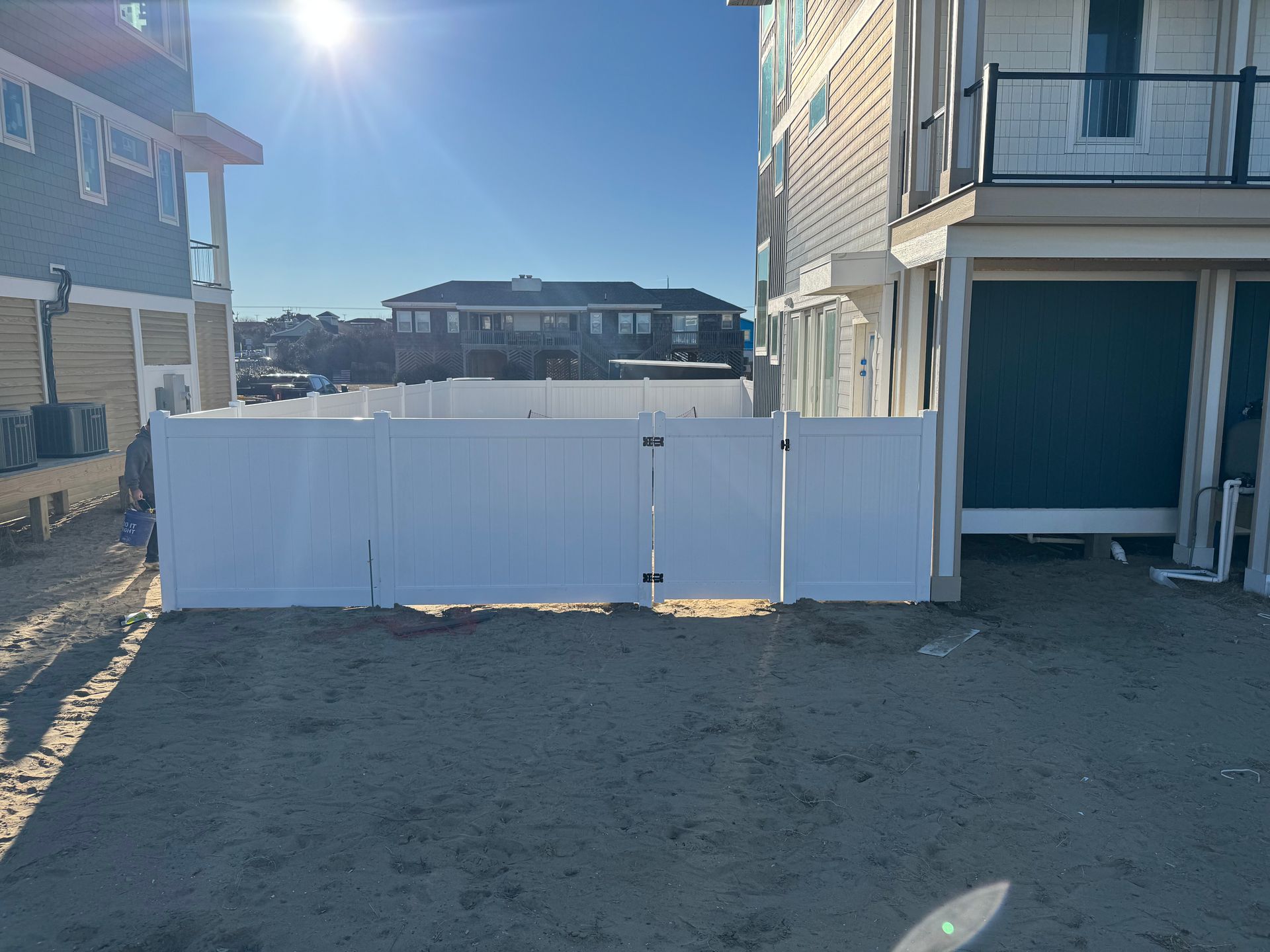 White fence between two buildings on a sandy surface under a sunny sky.