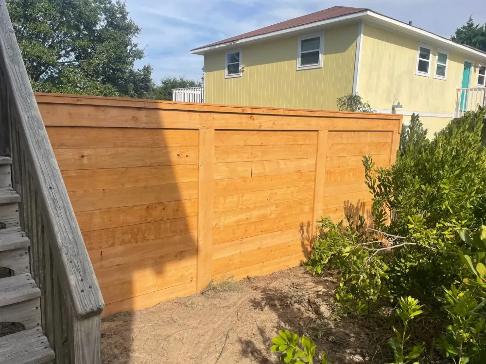 Wooden fence in front of a yellow house, with steps on the left and bushes on the right. Wooden fence in front of a yellow house, with steps on the left and bushes on the right.