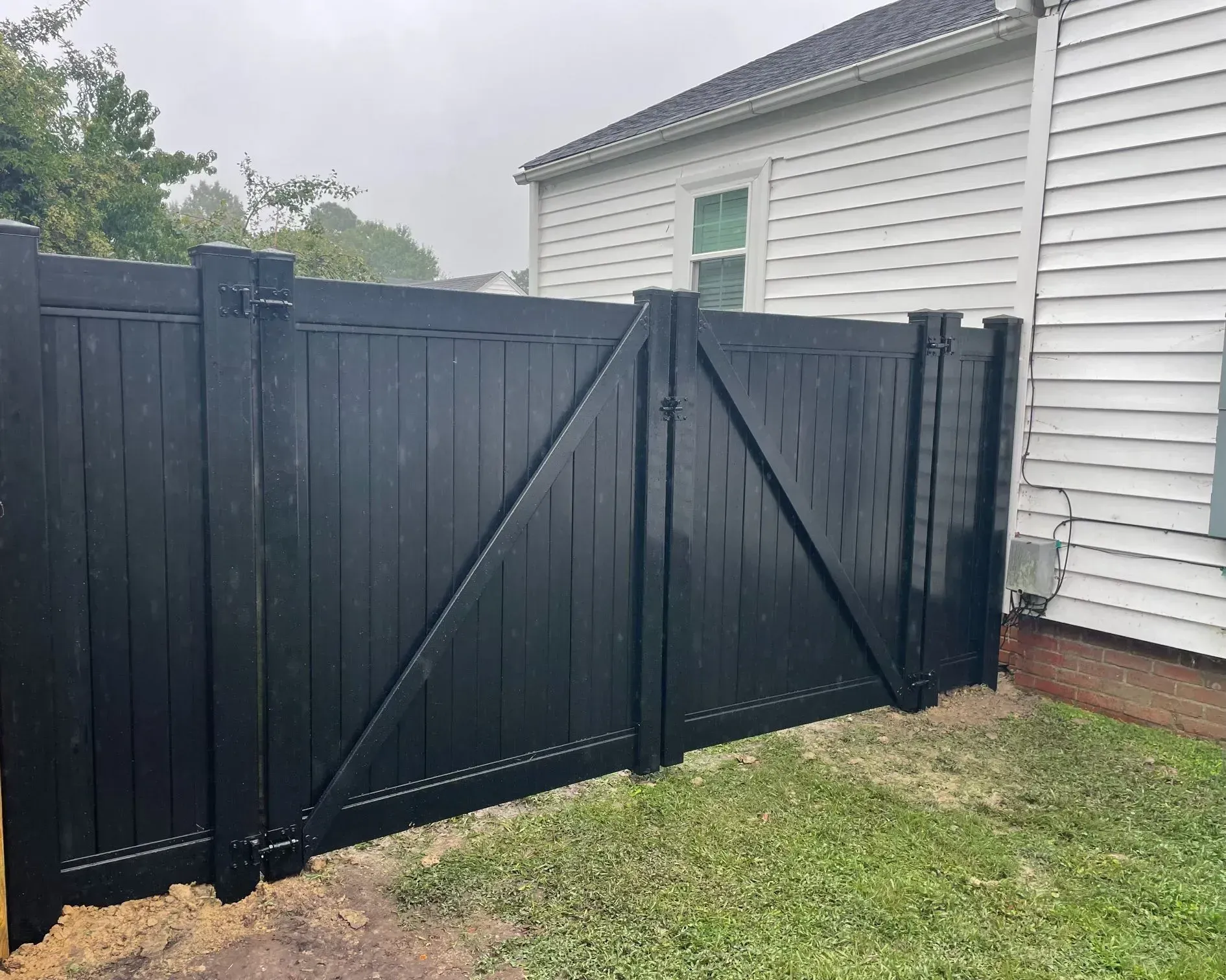 Black wooden fence with a gate, next to a white house, on green grass. Black wooden fence with a gate, next to a white house, on green grass.
