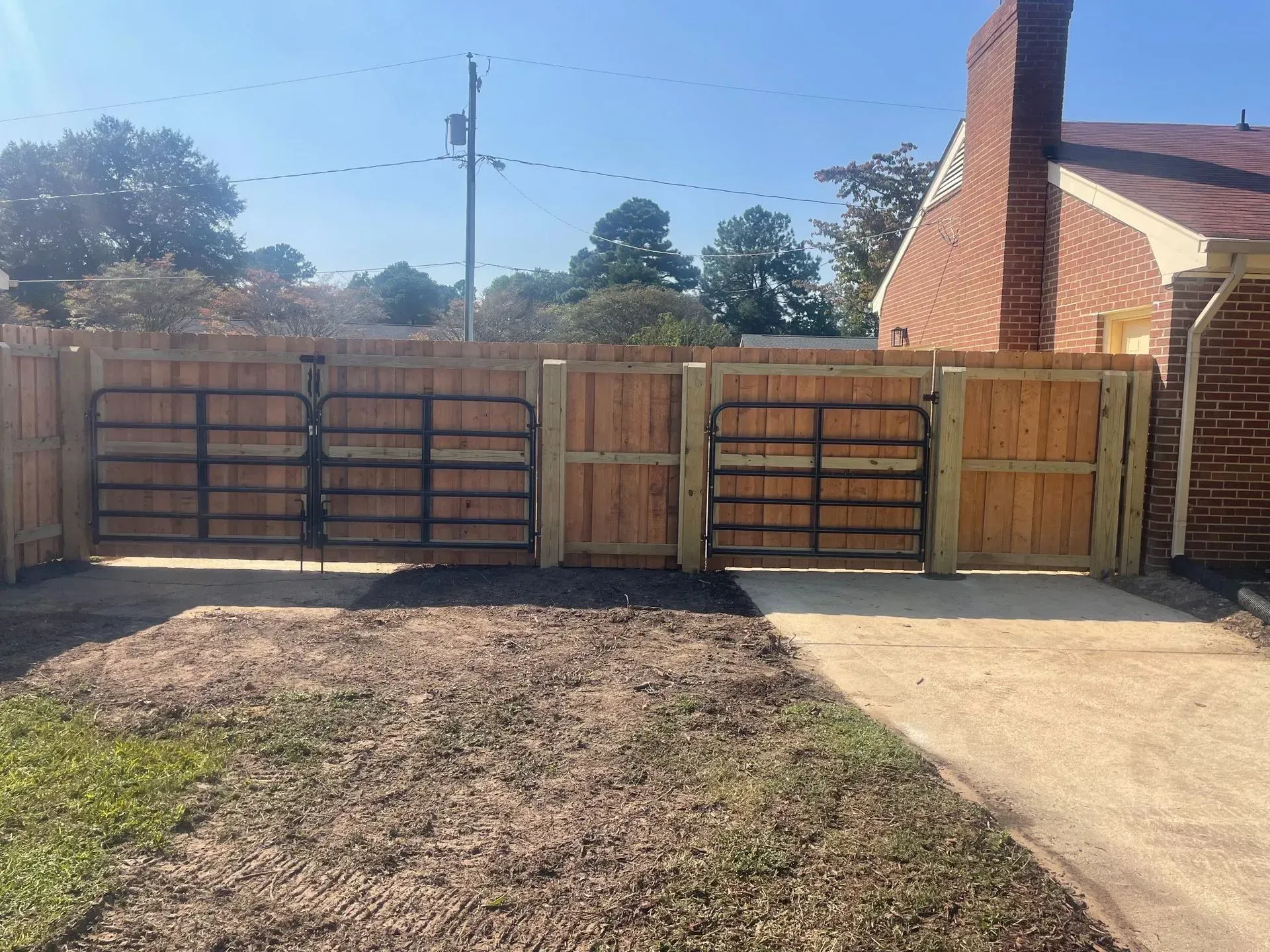 Black wooden fence with a gate, next to a white house, on green grass. Black wooden fence with a gate, next to a white house, on green grass.