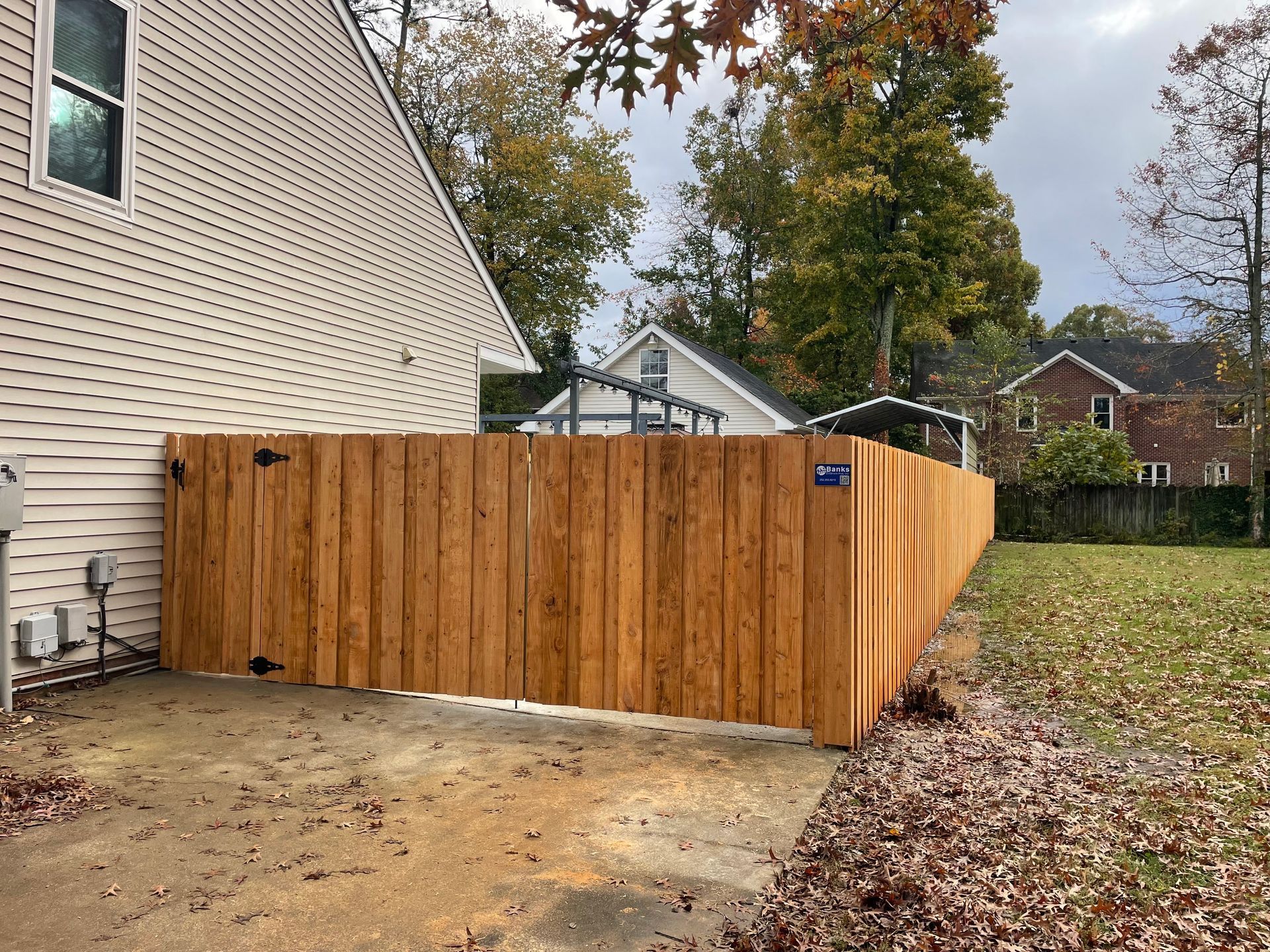 Wooden fence next to a house with a concrete area, autumn leaves.