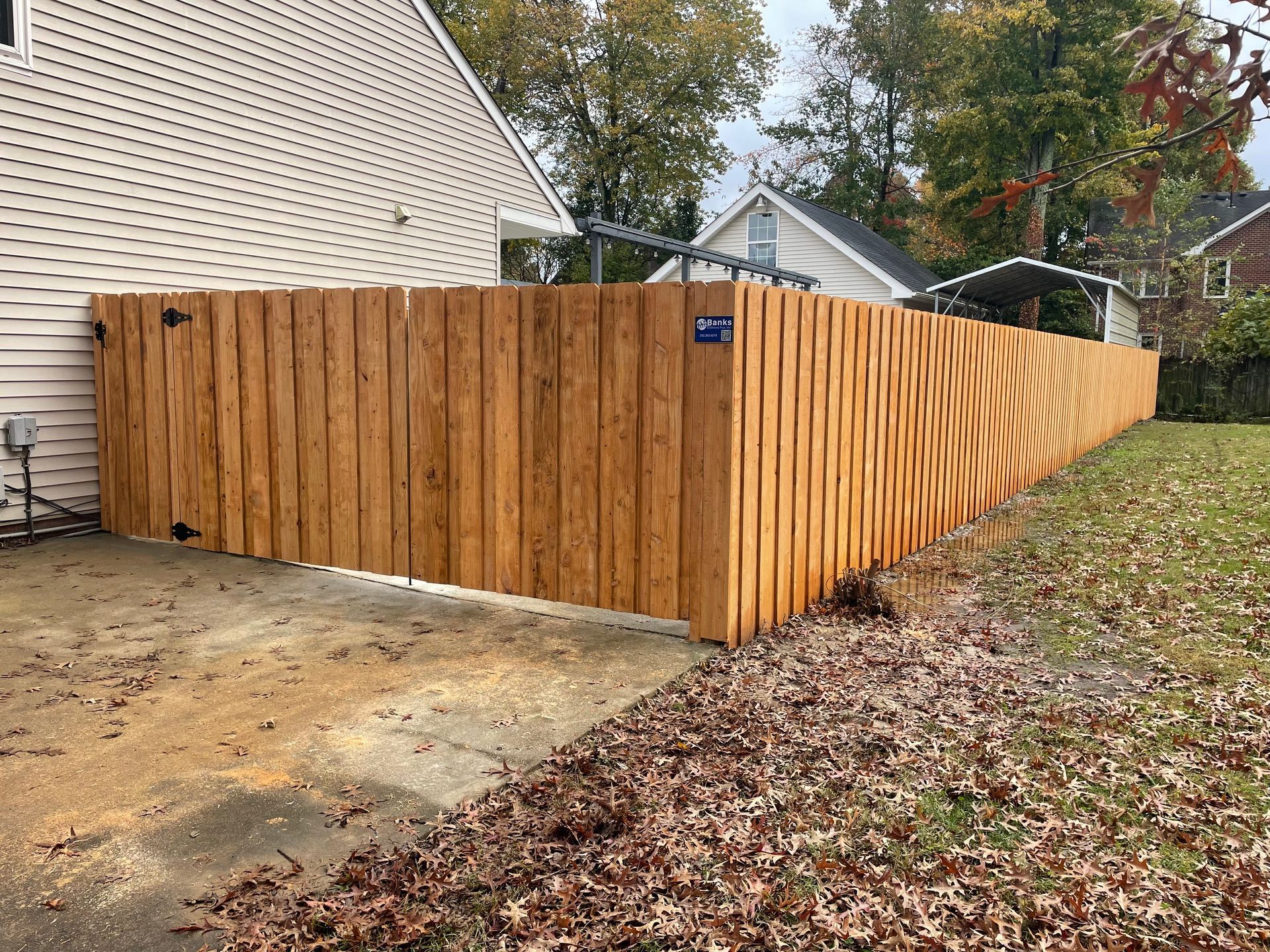 Wooden fence in a yard next to a house and driveway.