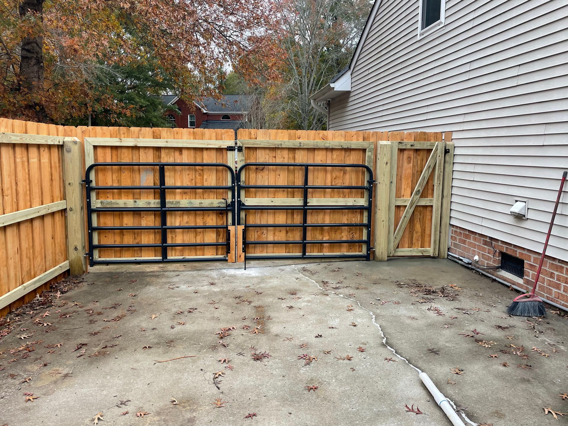 Wooden fence with double black metal gates and single door gate, on concrete ground.