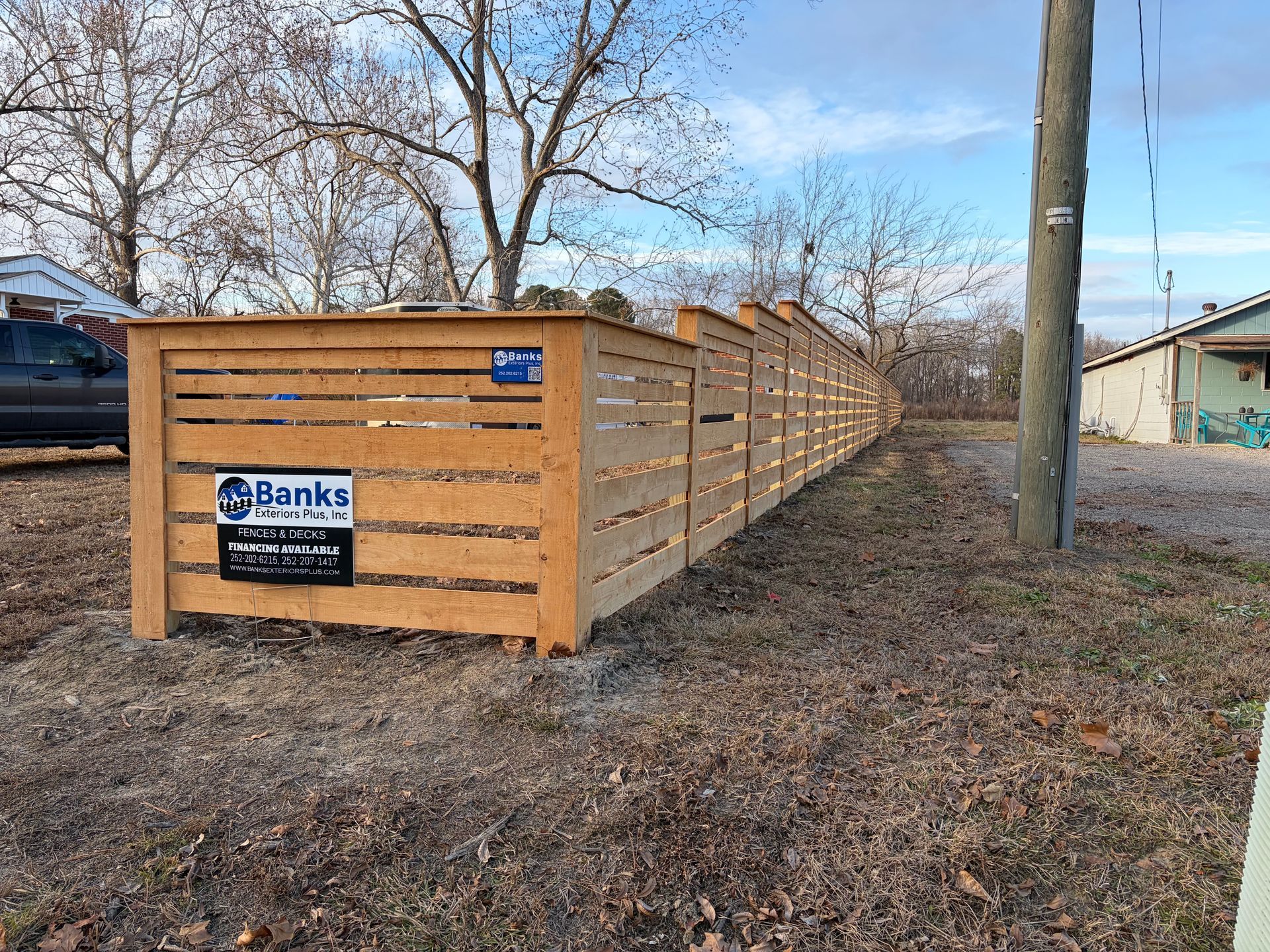 Wooden horizontal slat fence in a yard, with a sign from Banks Fencing.