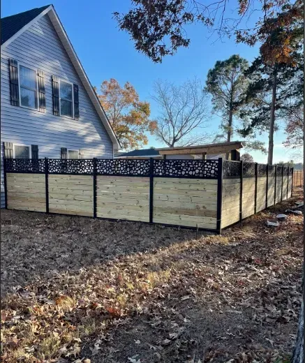 A wooden and black metal fence surrounds a house on a sunny day.