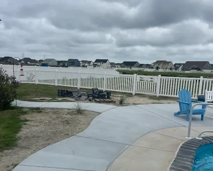 Flooded suburban neighborhood. Overcast sky, white fences, concrete patio with blue chair.