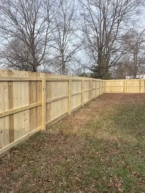 Wooden fence surrounding a grassy yard with bare trees in the background.