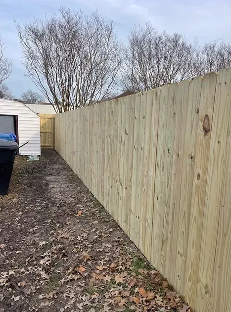 Wooden privacy fence in a backyard, alongside a dirt path and a small shed.