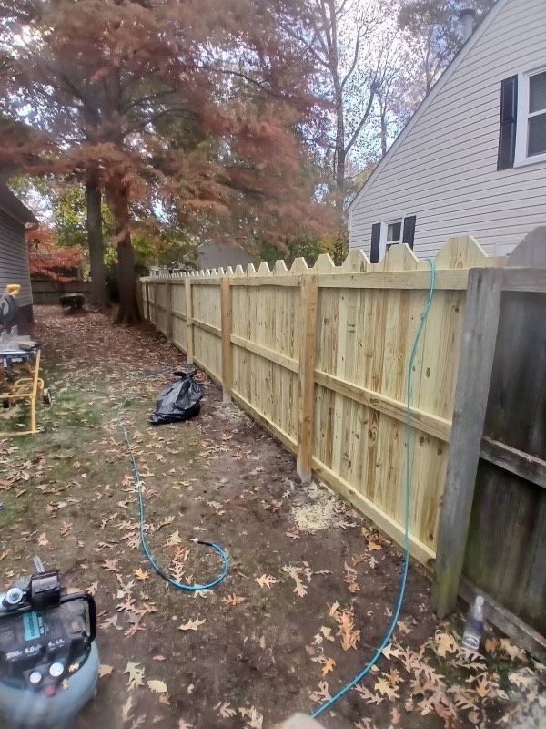 A newly constructed wooden fence with decorative tops, bordering a backyard.