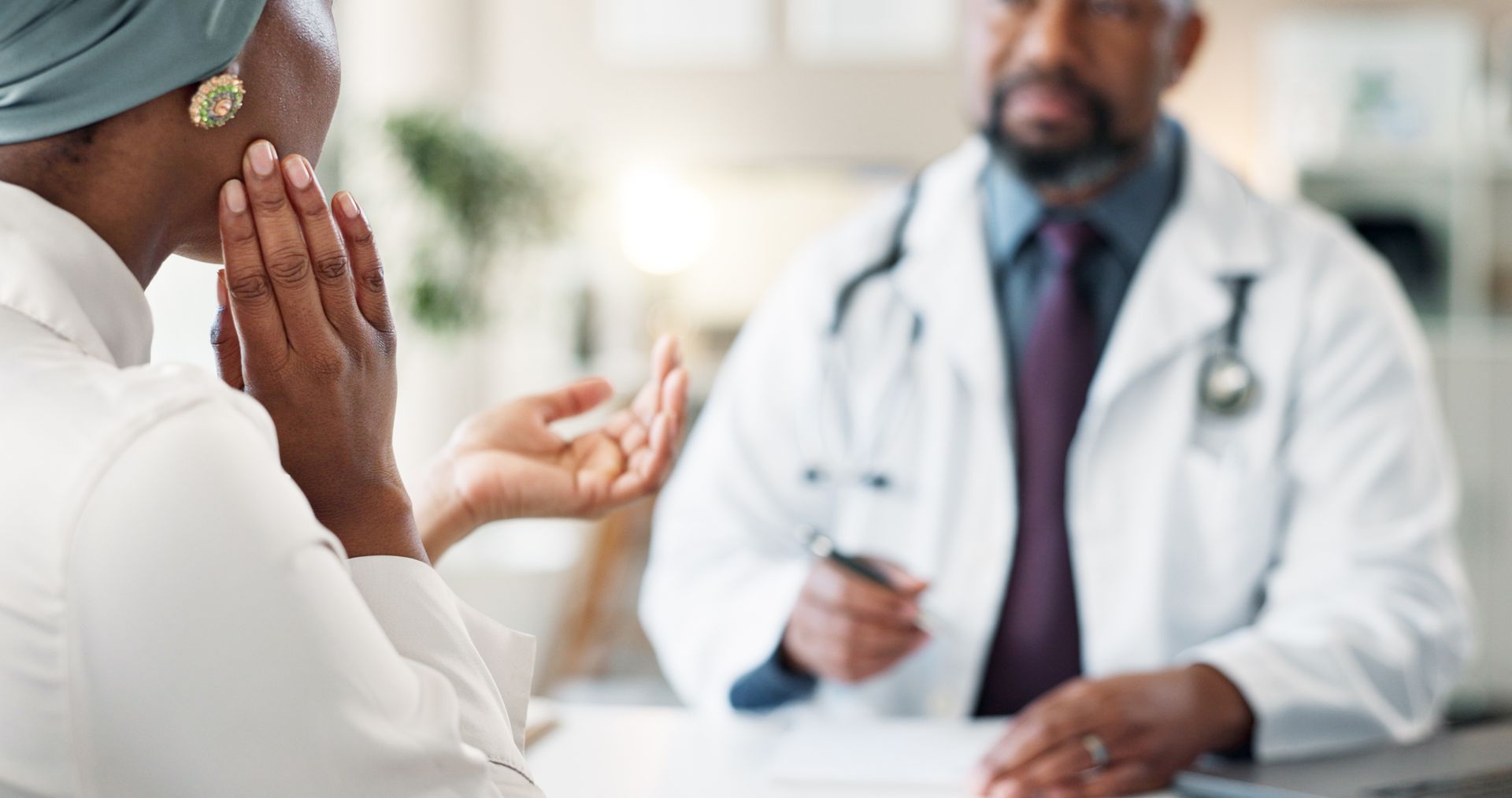 Woman touches her jaw while consulting with a doctor about TMJ pain and treatment options in clinic.