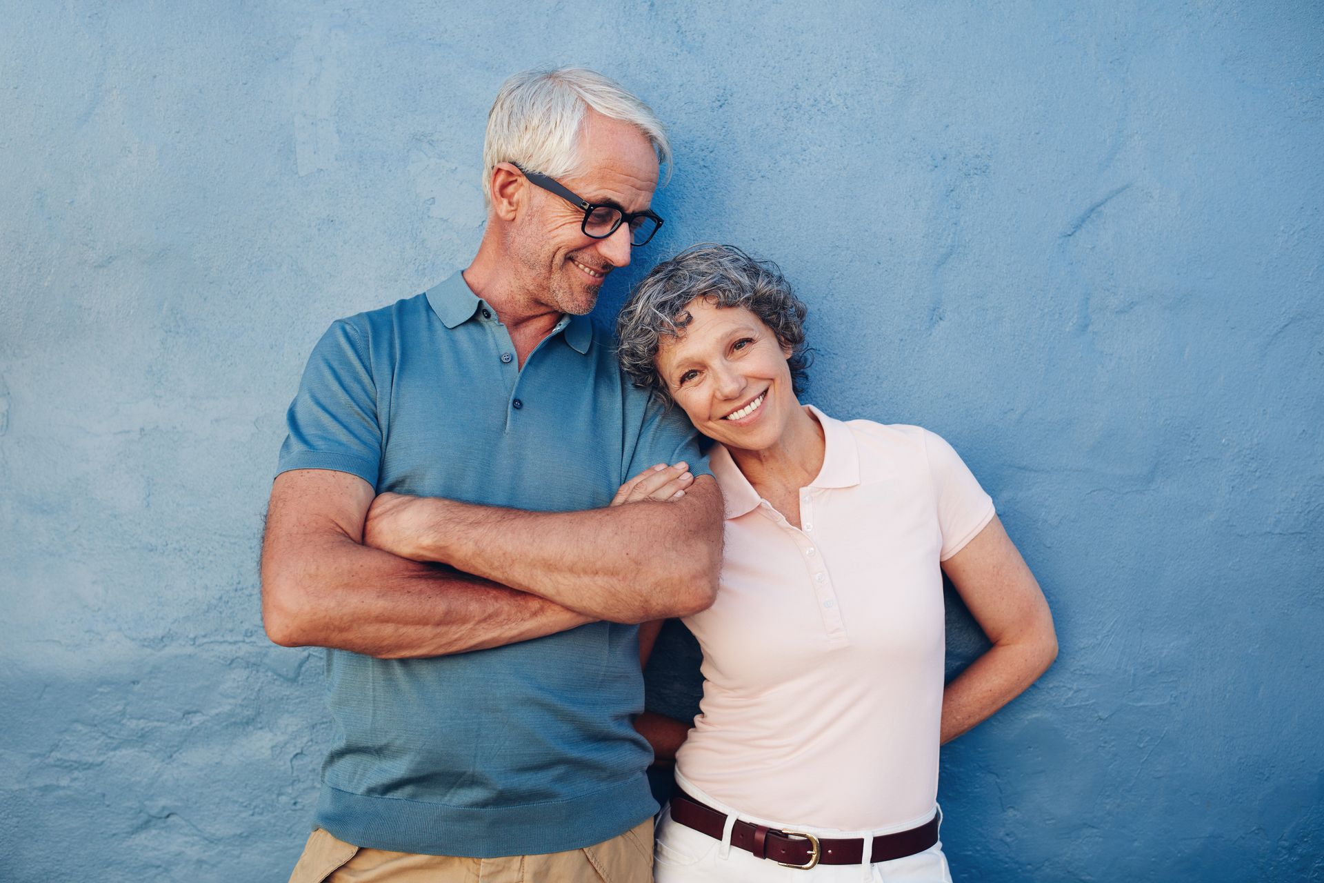 Smiling senior couple standing against a blue wall, showing confidence and happiness.