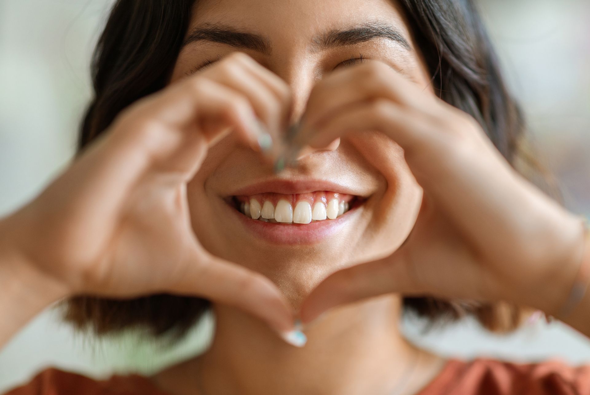 Woman smiling with healthy teeth, hands forming a heart shape to show happiness and good dental care