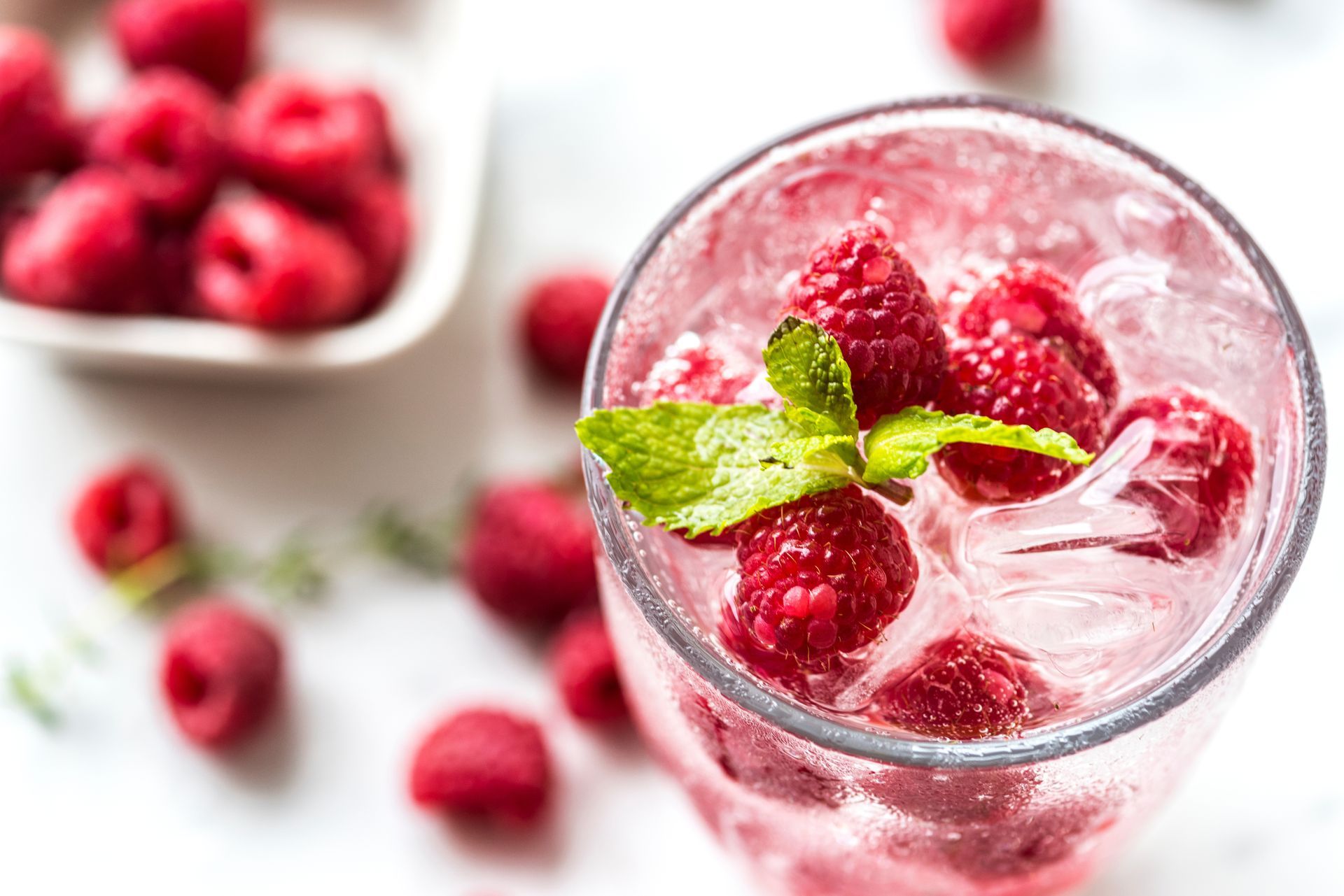 Refreshing glass of sparkling raspberry drink with ice cubes, fresh raspberries, and mint garnish.