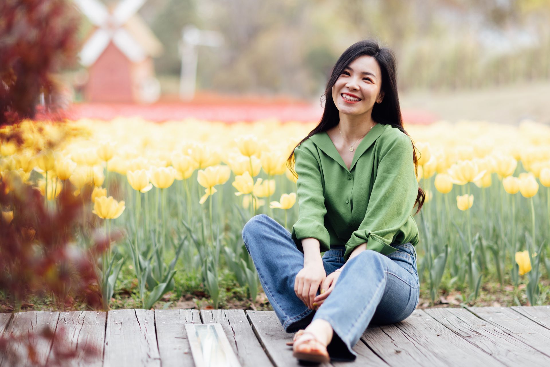 Smiling woman sitting on wooden path in a field of yellow tulips on a sunny day.
