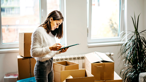 A woman surrounded by brown boxes and holding a checklist.