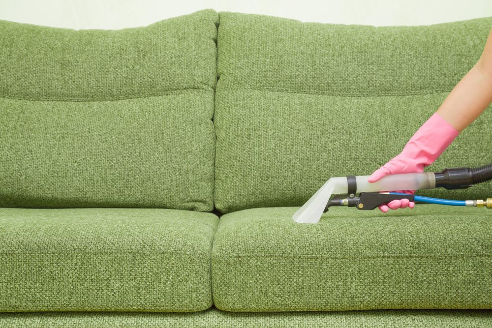 A Person is Cleaning a Green Couch With a Vacuum Cleaner — Dawsons Cleaning Specialist In Mount Louisa, QLD