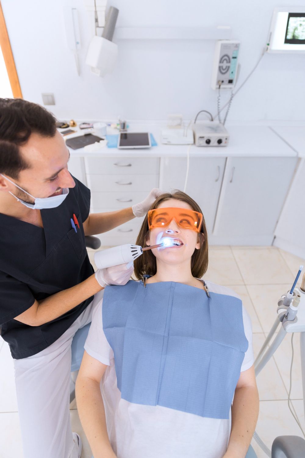 A woman is sitting in a dental chair getting her teeth whitened by a dentist.