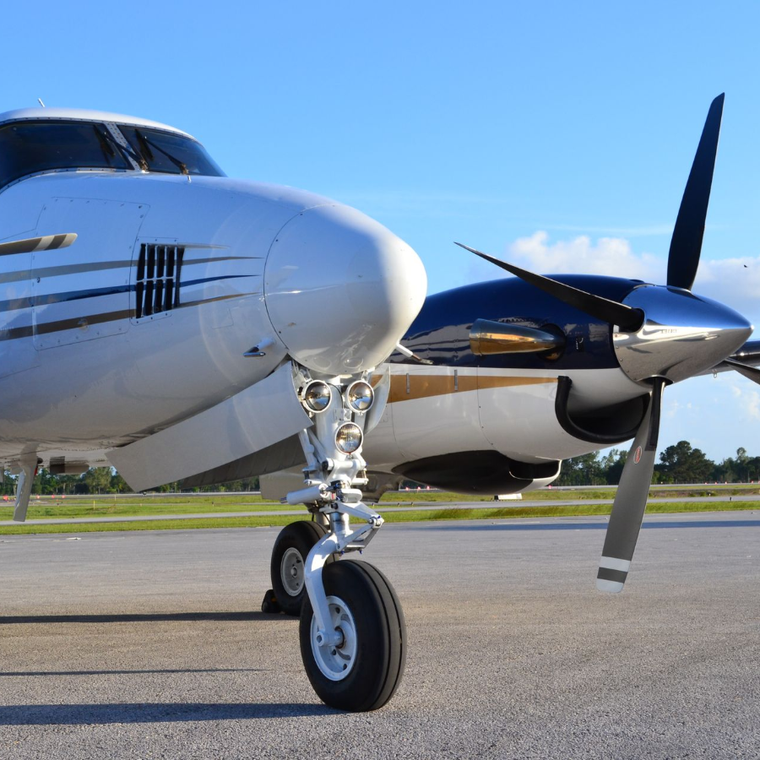 Silver twin-engine propeller airplane on a runway under a clear blue sky