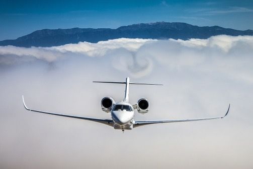 Small jet flying above clouds with mountains in the distance