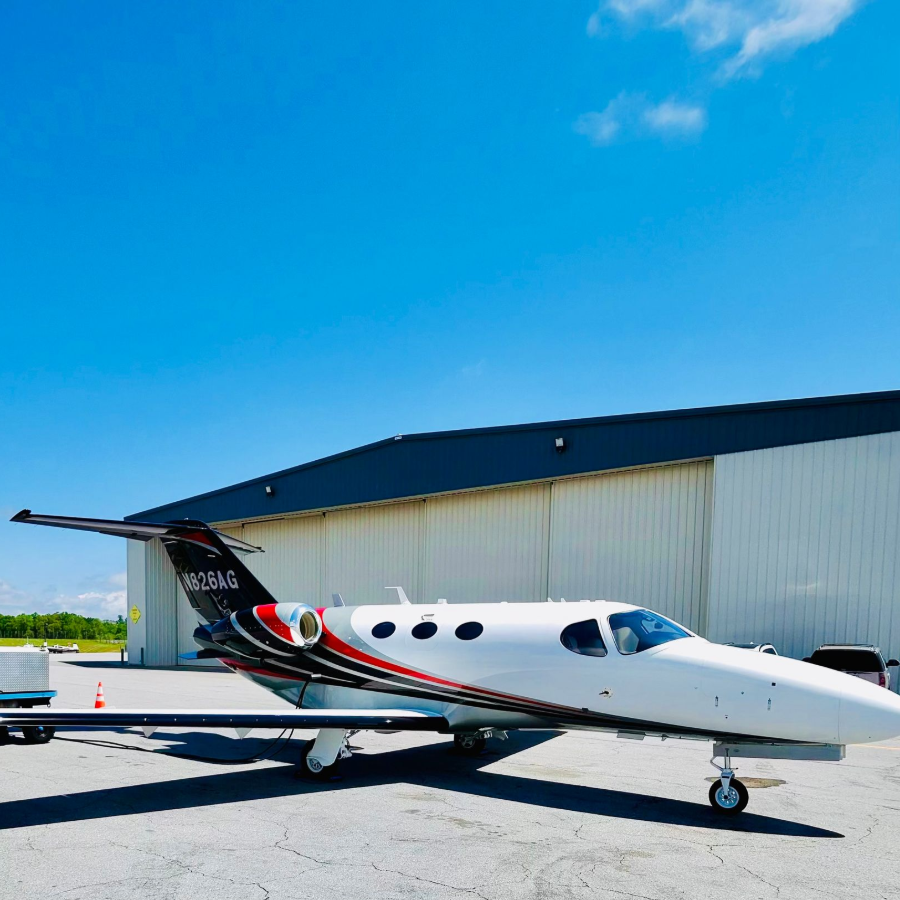 Small white private jet parked on a runway beside a hangar under a blue sky