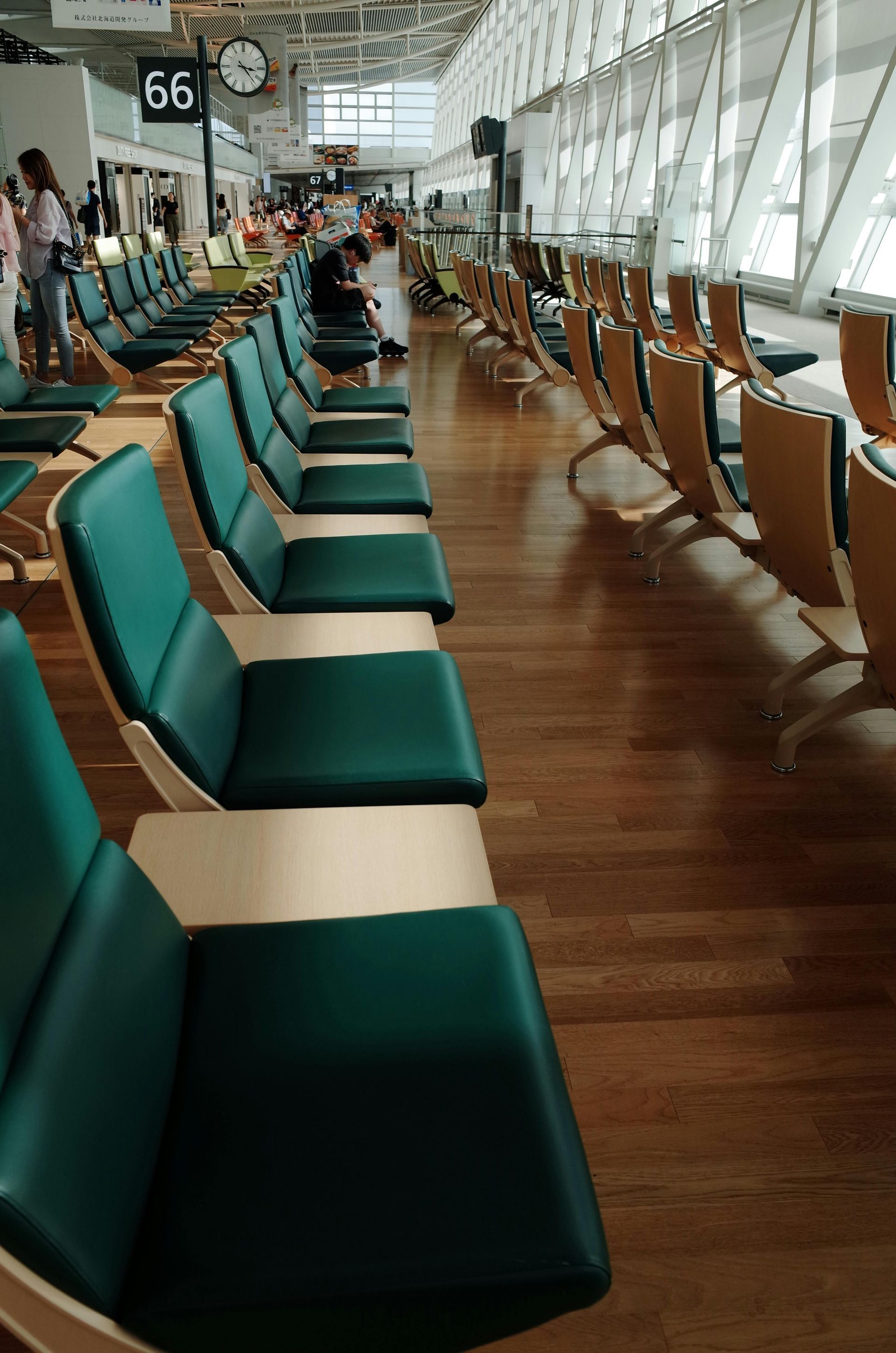 Empty airport waiting area with teal seats and large windows overlooking the runway.