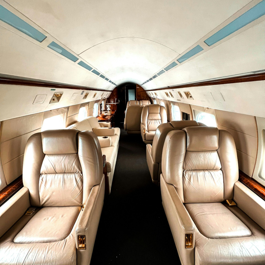 Inside a small private jet cabin with beige leather seats and a black aisle