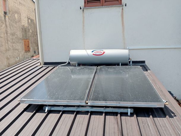 Scaldabagno solare sul tetto con due pannelli piani e un serbatoio cilindrico addossato a una parete