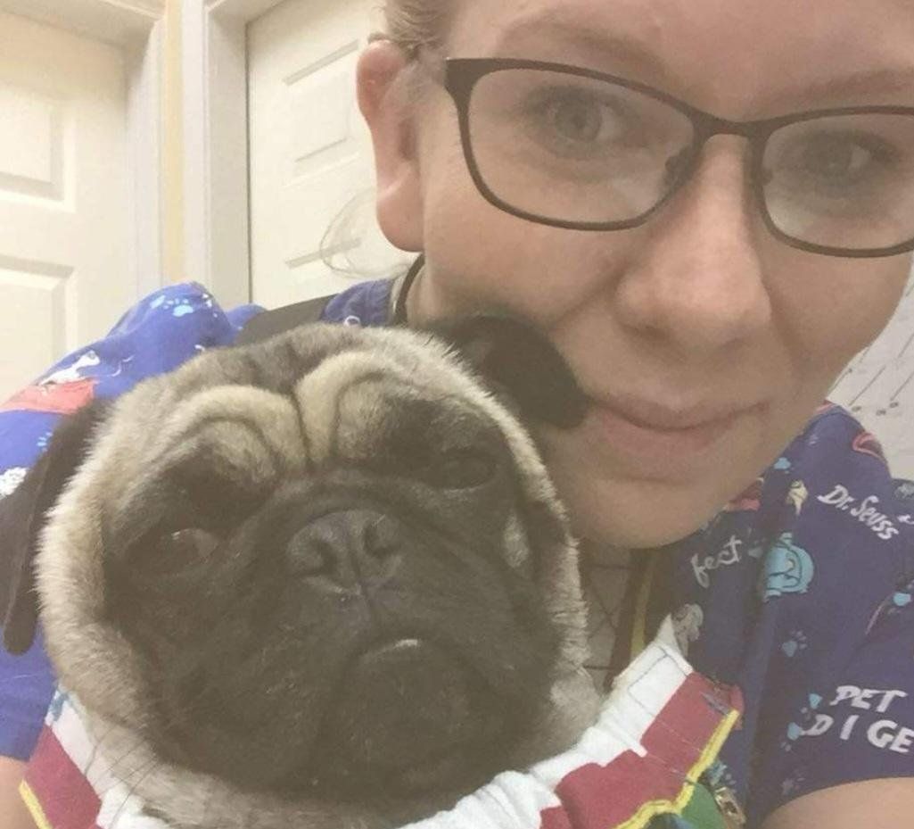 A woman wearing glasses is holding a pug dog