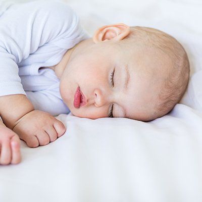 A baby is sleeping on a bed with his eyes closed