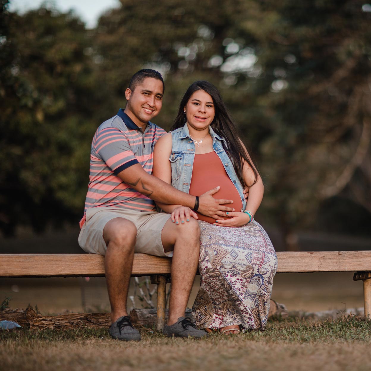 A man and a pregnant woman are sitting on a wooden bench.