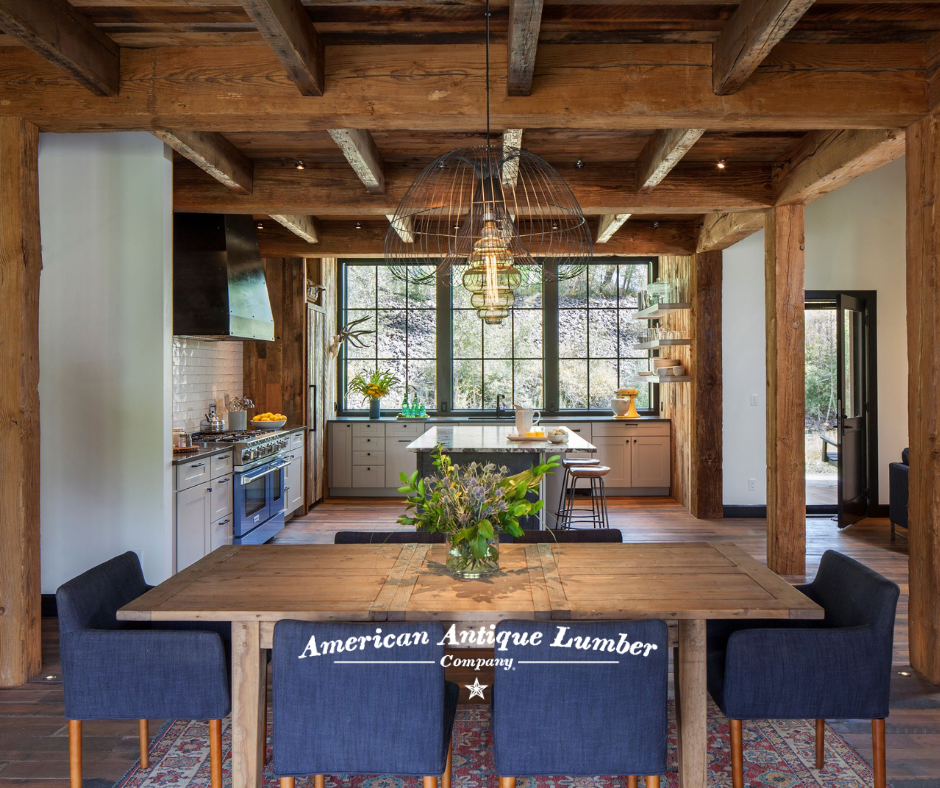 Wooden kitchen table surrounded by blue chairs in front, behind a center island and wall of windows. 