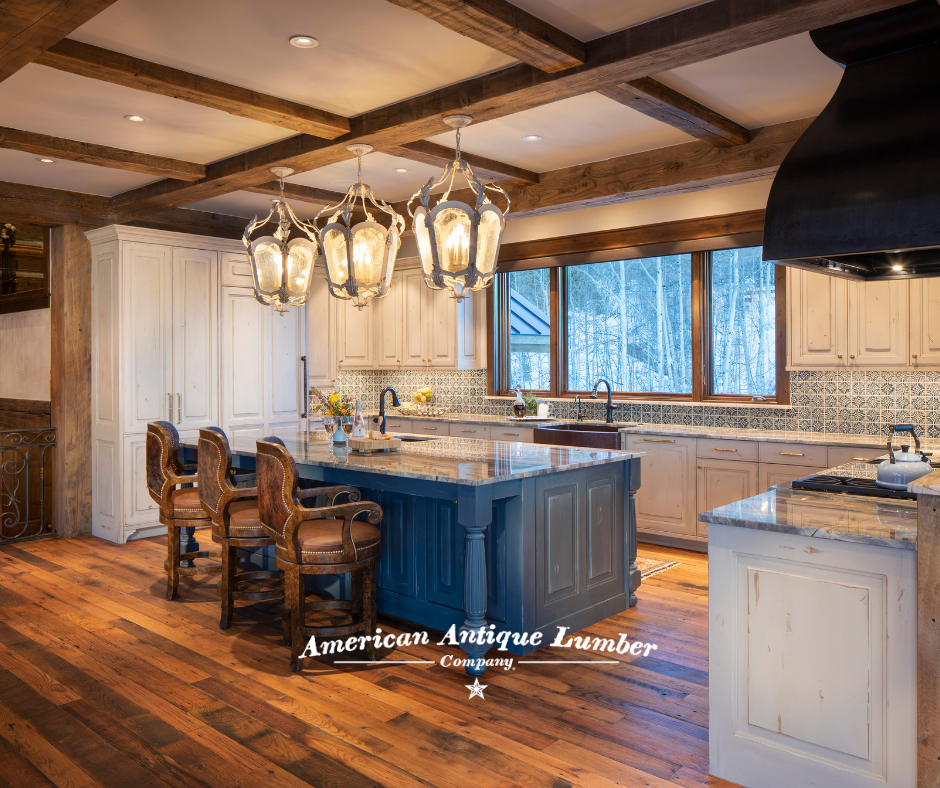 White kitchen cabinets, reclaimed wood floors, blue center island with three large white metal lights and three large wooden chairs.