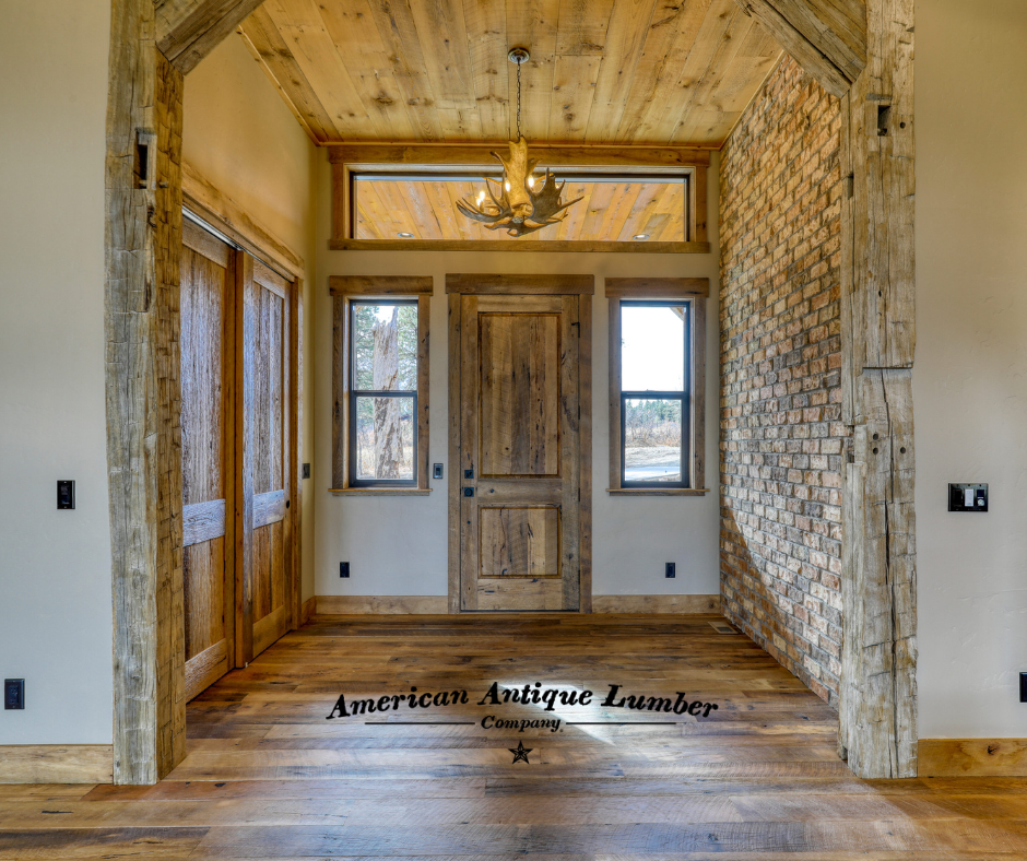 Interior entryway to a home showing the reclaimed wood door with windows above and to the side. An antler chandelier hangs above with a brick wall on the right.